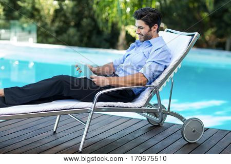 Smart man relaxing on sun lounger and using a digital tablet near the pool