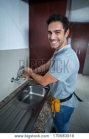 Portrait of smiling man fixing faucet with wrench in kitchen