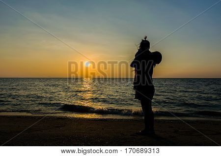 Silhouette of women and children stand watching sunset on the beach with the sea.