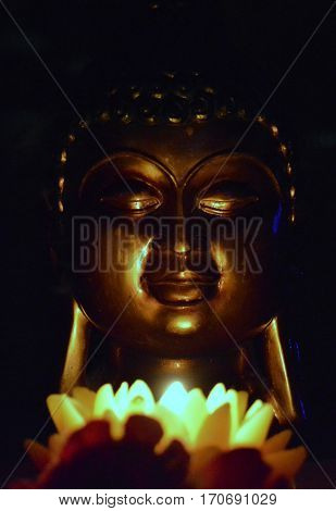 Buddha head in the dark, illuminated by a candle in the form of a lotus flower.