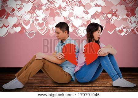 Sad couple holding broken heart pieces against gray concrete wall