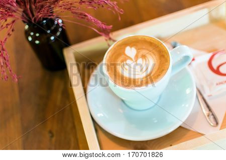 A cup of coffee latte art in Rosetta pattern with tree or flower in glass bottles on wooden background.