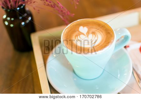 A cup of coffee latte art in Rosetta pattern with tree or flower in glass bottles on wooden background.