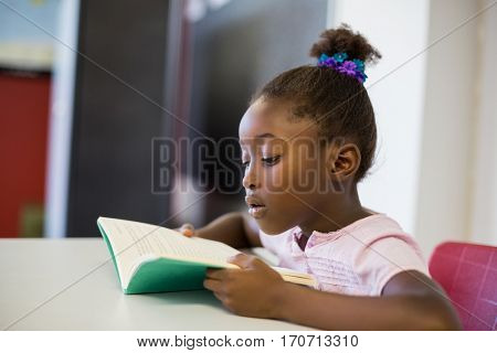 School girl reading book in classroom at school