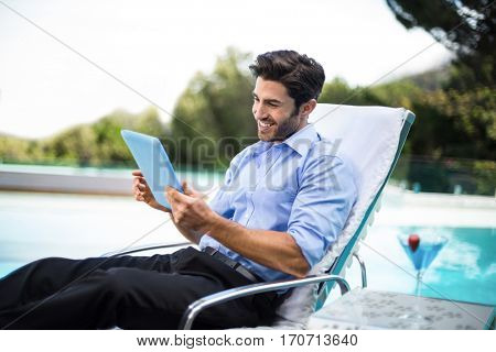 Smart man relaxing on sun lounger and using a digital tablet near the pool