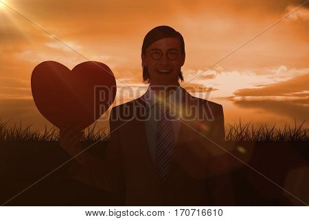 Geeky businessman smiling and holding heart card against a couldy day