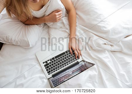 Cropped image of woman using laptop and lying on bed. Top view