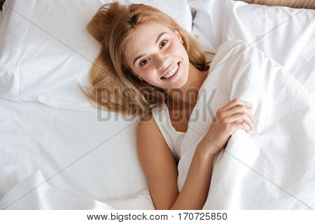 Top view of pretty woman lying on bed and looking at camera