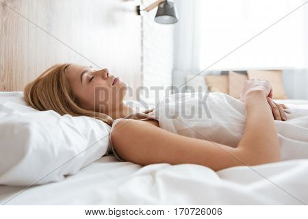 Side view of young woman sleeping on bed with crossed arms in bedroom