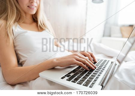 Cropped image of woman lying on bed with laptop in bedroom. Side view