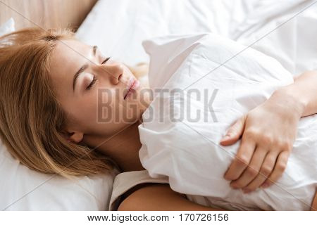 Close up image of young woman sleeping on bed and embracing with pillow