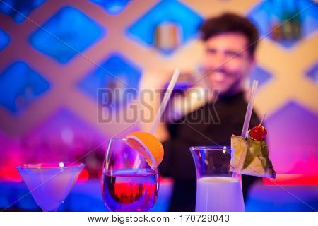 Various drinks on counter while barkeeper in background at bar