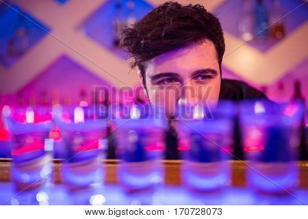 Bartender looking at shot glasses on illuminated bar counter