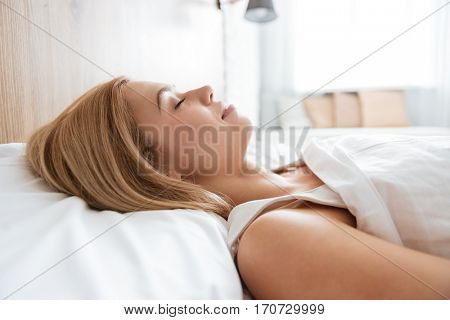 Close up image of young woman sleeping on bed in bedroom with window on background