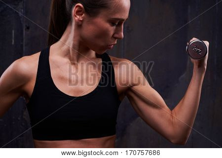 Extreme close-up of pertinacious muscular fitness woman with dumbbell pumping up biceps. Exercises for abdomen, fitness girl hands holding dumbbells showing her biceps