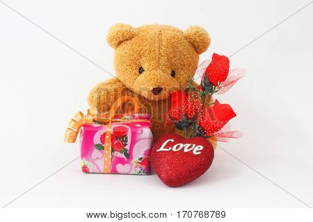 Brown teddy bear with a red rose and a gift box on a white background.