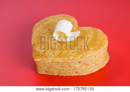 Pile of pancakes in the shape of a heart on red background with flake of butter