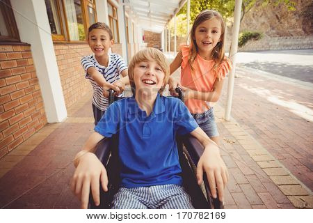 Portrait of school kids pushing a boy on wheelchair in school corridor