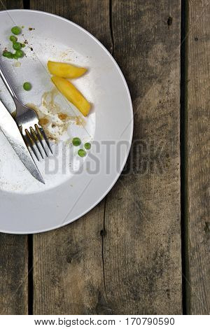 Overhead view of leftovers on a plate with knife and fork on a rustic wooden background