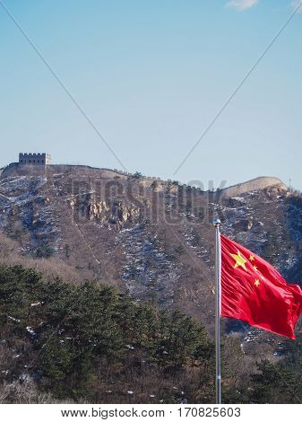 A bright red Chinese flag waves in front of the Great Wall of China.