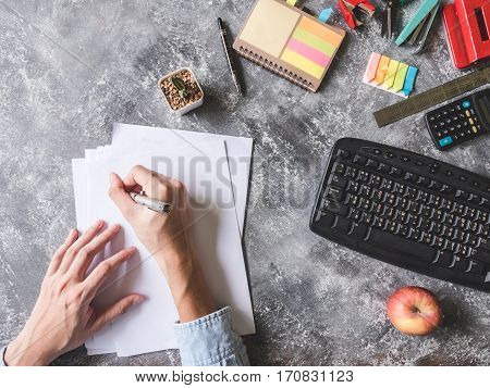 Top view of Male hands writing on paper sheet with Office supplies on Grunge gray background