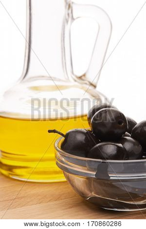 Glass cruet with Extra virgin olive oil, canned black olives in bowl stand on a wooden cutting board on a white background.
