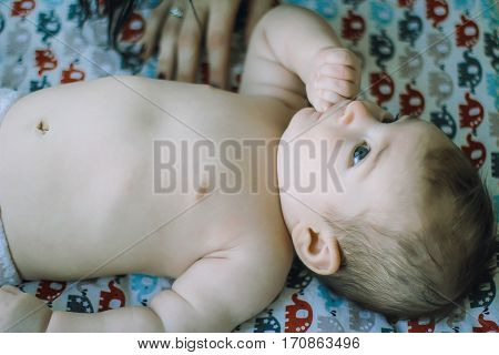 little baby lying on the bed in the diaper. thumb-sucking
