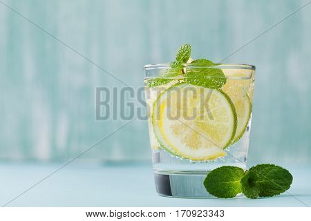 Mineral infused water with limes, lemons, ice and mint leaves on blue background. Homemade detox soda recipe.