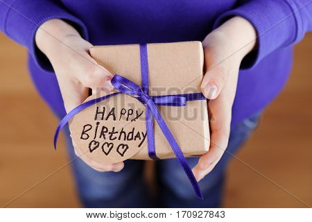 Childrens hands holding a gift or present in kraft paper and tag with note Happy Birthday. Holiday concept, top view.