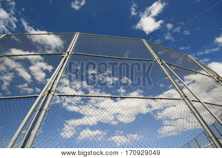 Upward view of the Backstop fencing of a baseball field under Blue Cloudy skies
