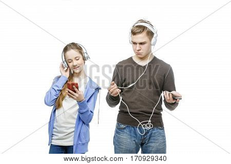 Beautiful teen age boy and girl in casual clothes standing on white background listening to music in headphones. School children. Isolated. Copy space.