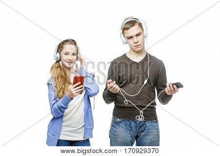 Beautiful teen age boy and girl in casual clothes standing on white background listening to music in headphones. School children. Isolated. Copy space.