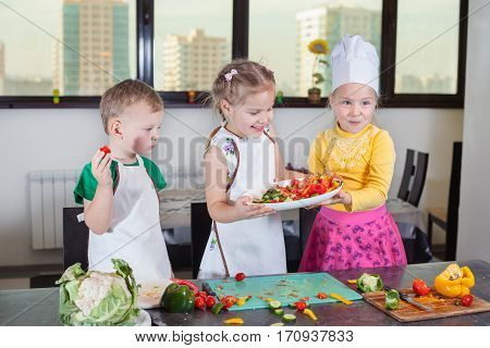 Three Cute Kids Are Preparing A Salad In The Kitchen