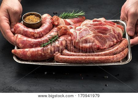 Male hands holding a iron tray with a meat for grilling. Sausages steak and cevapi on a iron tray close up