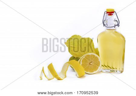 Open glass decanter bottle and shot glass filled with yellow lemon liquor or limoncello or limoncino on white. Peeled natural organic lemon.