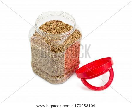 Buckwheat groats peeled from the husk in the transparent plastic container with a red open cover on a light background