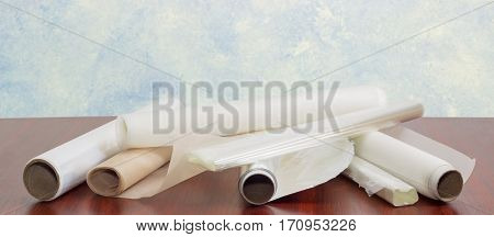 Several rolls of the plastic oven bags plastic food wrap aluminum foil and various parchment paper for household use closeup on a dark red wooden table