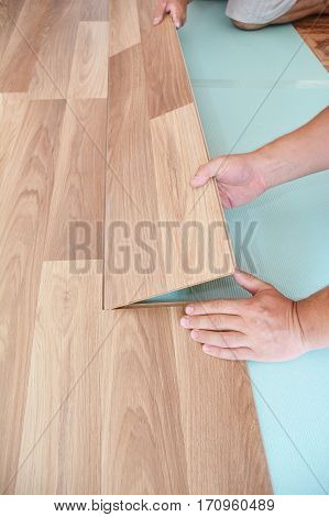 Contractor installing wooden laminate flooring with insulation and soundproofing sheets. Man laying laminate flooring. Man laying laminate flooring. Step by Step.
