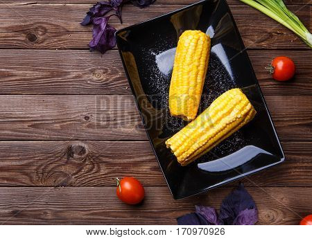 Corn on the black plate on wooden table. Helthy food.