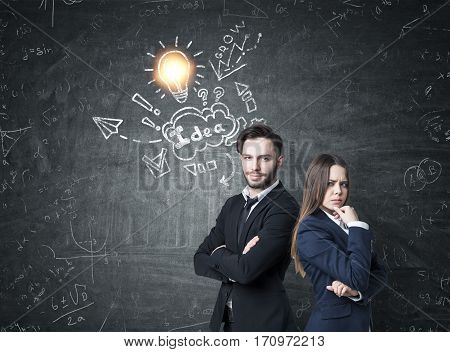 Portrait of a businessman with crossed arms and his female business partner standing near a blackboard with a business idea skech drawn on it.