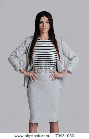 Modern woman. Gorgeous young woman in smart casual wear keeping hands on hip and looking at camera while standing against grey background