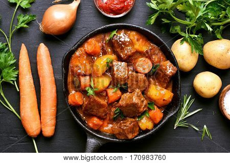Goulash beef stew and ingredients on dark background top view