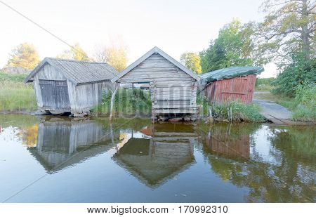 Old boathouse made of gray timber and planks reflecting in the water in the swedish archipelago