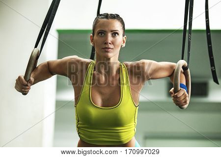 Young fit woman pulling up on gymnastic rings.