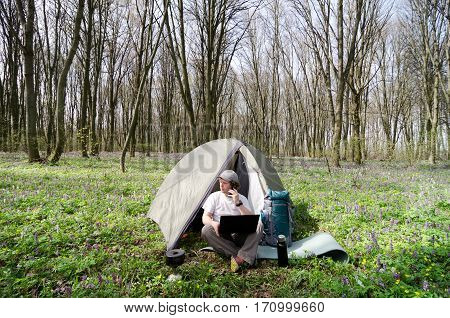 A man working on a laptop outdoors in a tent camp.