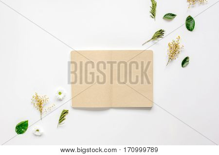 Flower petals and brown craftpaper copybook on white table background top view mock up