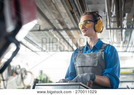 Woman worker operating a machine tool in metal workshop or factory in a diligent manner