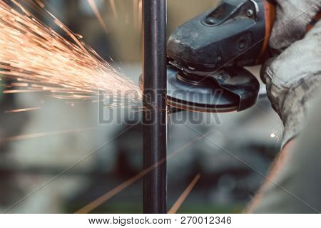 Worker in metal factory grinding workpiece with disk grinder, sparks flying