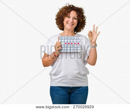 Middle ager senior woman holding menstruation calendar over isolated background doing ok sign with fingers, excellent symbol