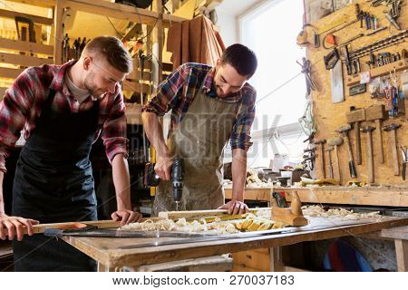profession, carpentry, woodwork and people concept - two carpenters with wooden board and electric drill working at workshop